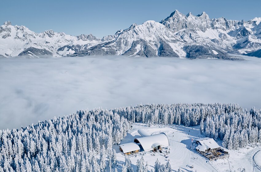 Snow-covered mountain lodge by forest edge with cable car and Alps above a sea of fog | © Bergbahnen Filzmoos GmbH