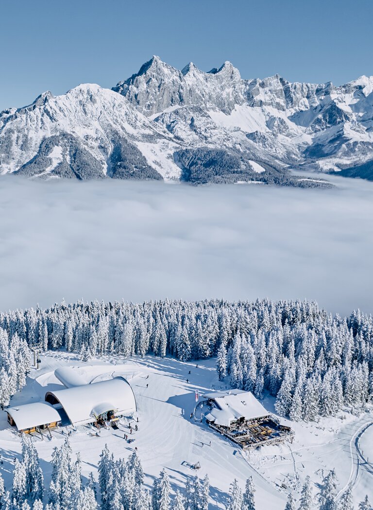 Snow-covered mountain lodge by forest edge with cable car and Alps above a sea of fog | © Bergbahnen Filzmoos GmbH