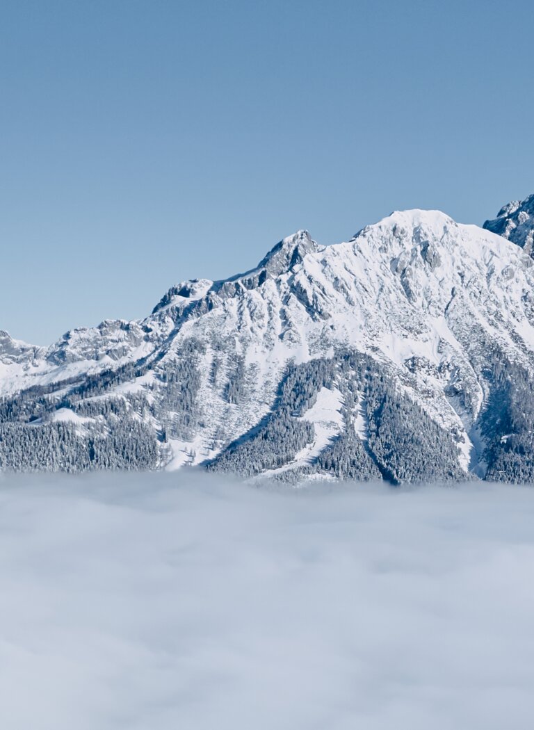 Snow-covered mountain lodge by forest edge with cable car and Alps above a sea of fog | © Bergbahnen Filzmoos GmbH