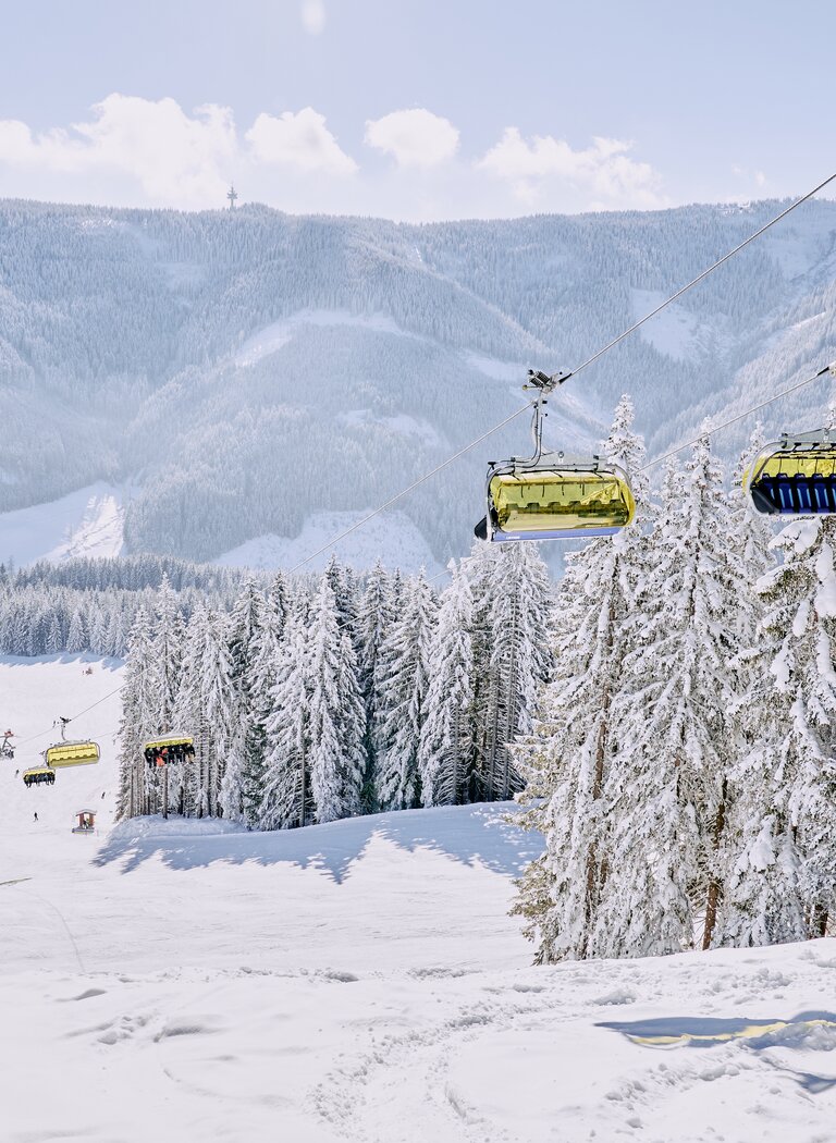 Yellow chairlifts move above wide ski slope with snowy trees and mountain scenery in background | © Bergbahnen Filzmoos GmbH