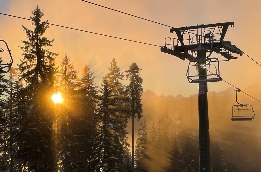Chairlift and snow-covered trees backlit by warm sunset glow shining through the forest. | © Bergbahnen Filzmoos GmbH