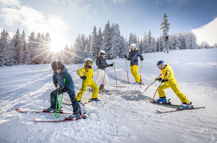 Five skiers stand with skis on a snowy slope before a winter forest and the low winter sun. | © Bergbahnen Filzmoos GmbH