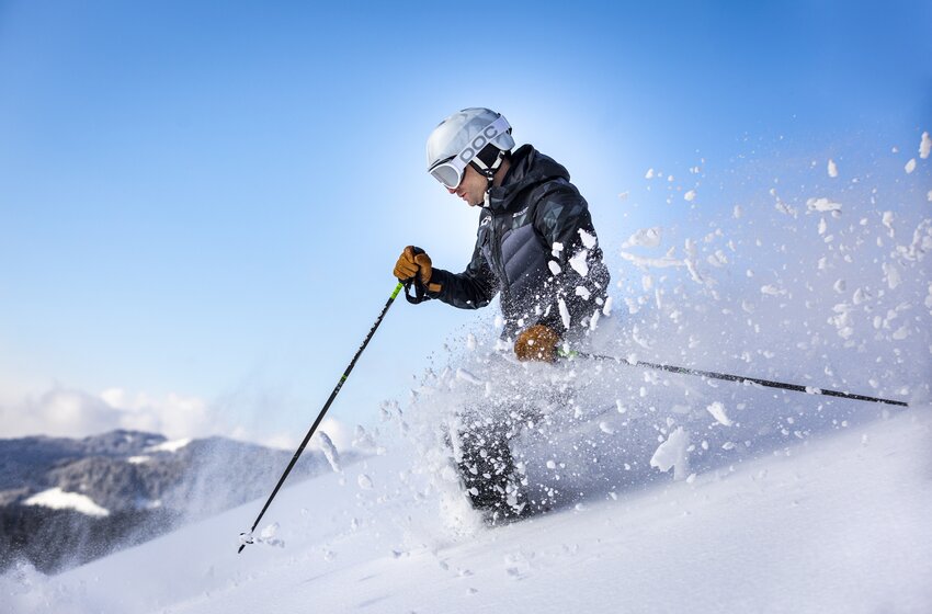 Skier with white helmet carves through fresh powder snow in sunlight, snow spraying to the side. | © Bergbahnen Filzmoos GmbH